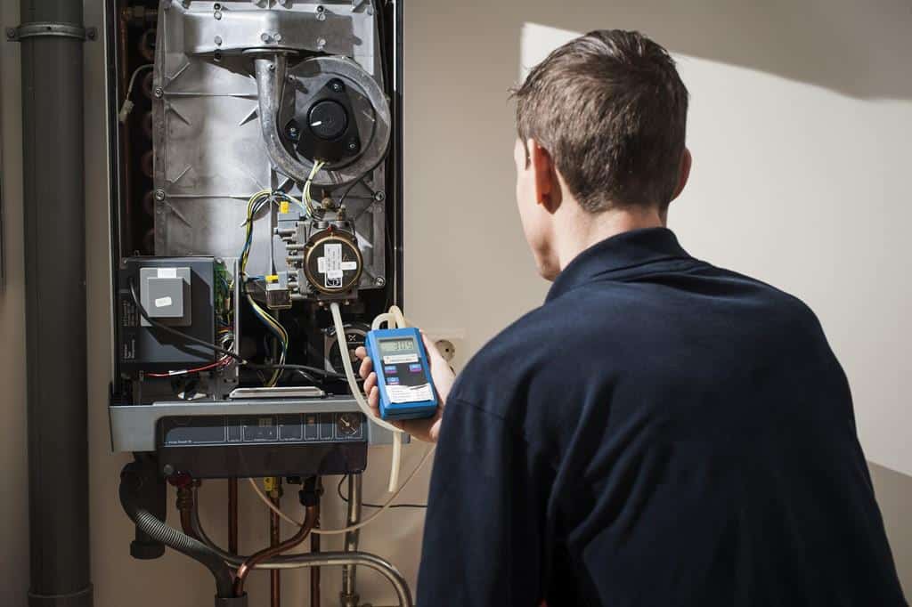 Cool Ducts HVAC technician taking diagnostic readings with a digital meter on a wall-hung gas water heater in a Northern Colorado home